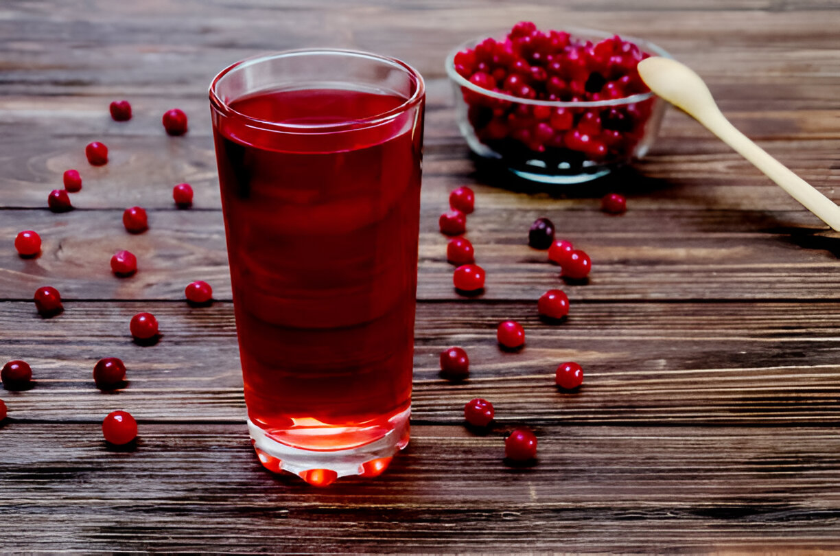 A glass of red berry drink beside scattered fresh berries on a wooden table.