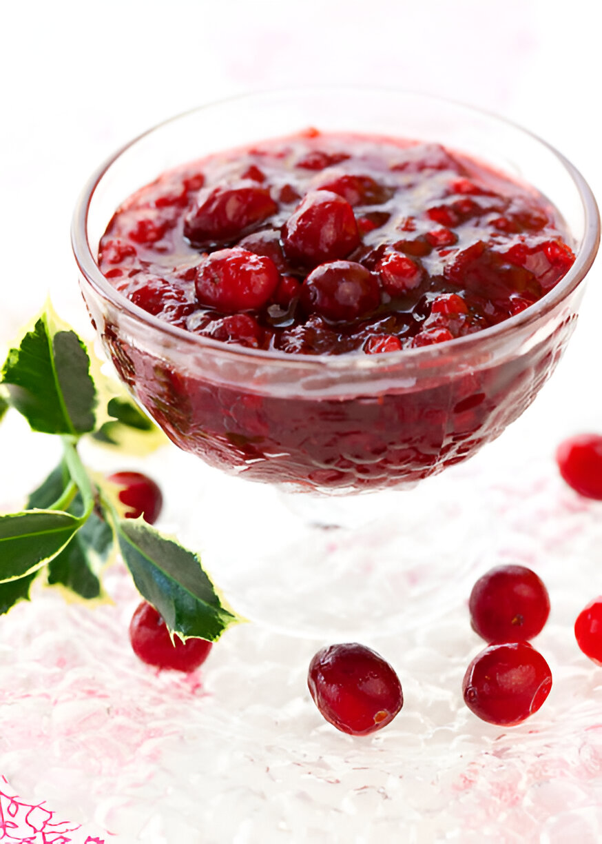 A glass bowl filled with cranberry sauce garnished with fresh cranberries and green leaves.