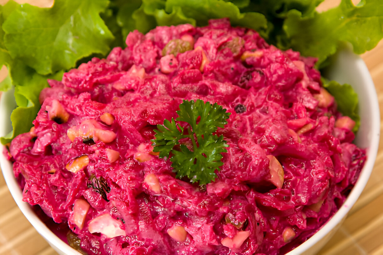 A vibrant pink salad served in a white bowl, garnished with a sprig of cilantro and surrounded by fresh green lettuce leaves.