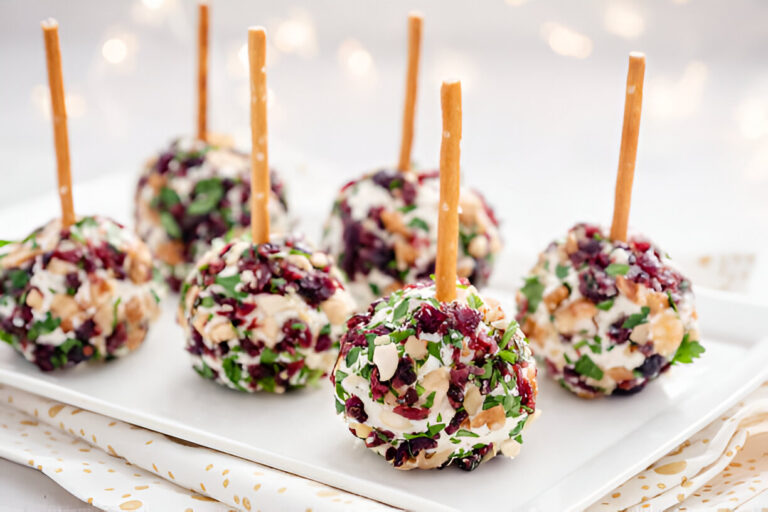 A platter of colorful cheese balls coated with nuts and herbs, each topped with a pretzel stick.