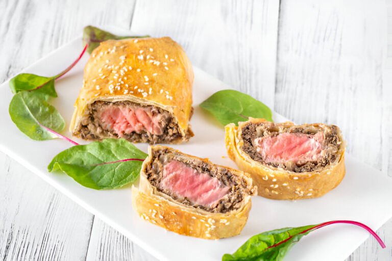 Slices of beef Wellington served on a white plate with greens.