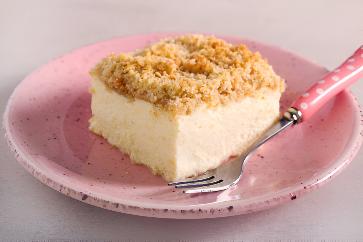 A slice of creamy dessert topped with a crumbly layer on a pink plate with a silver fork.