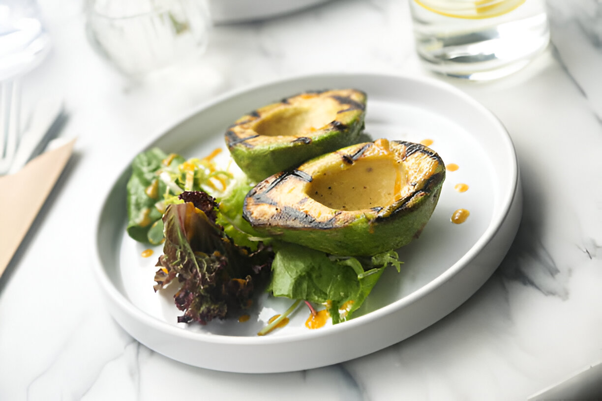 Grilled avocado halves served on a white plate with salad greens