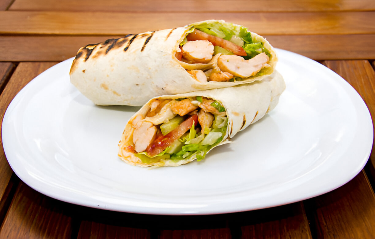 Two grilled chicken wraps with fresh vegetables on a white plate.