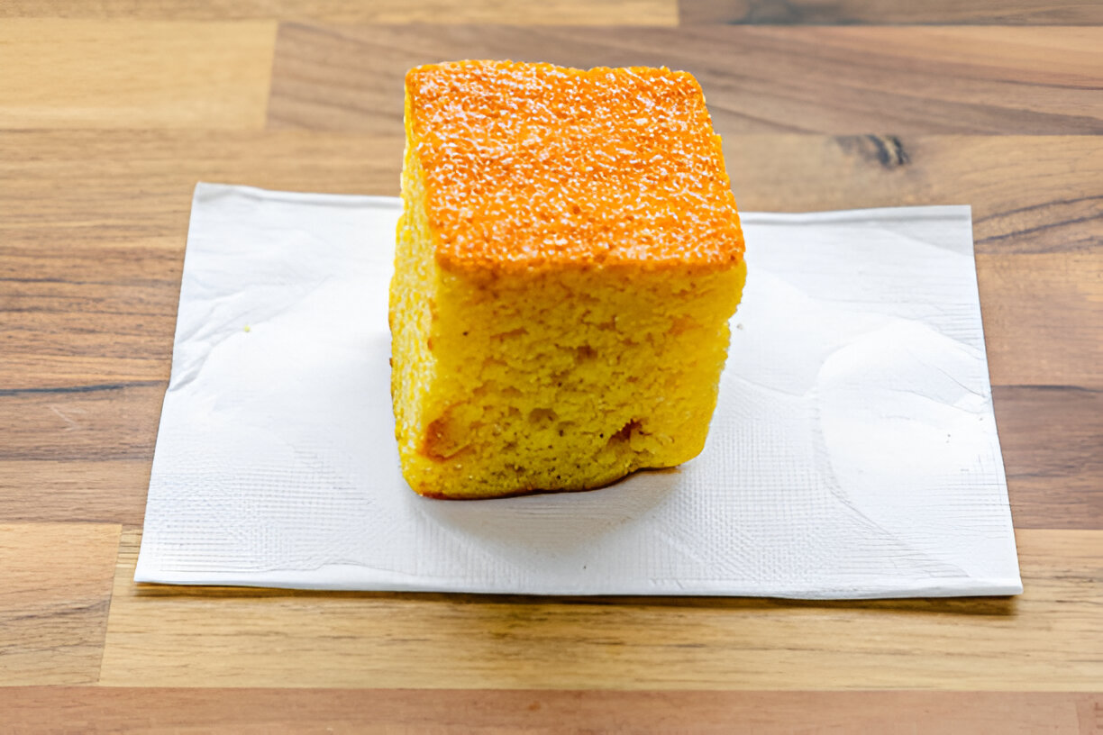 A square slice of yellow cake with a shiny golden top on a paper napkin.
