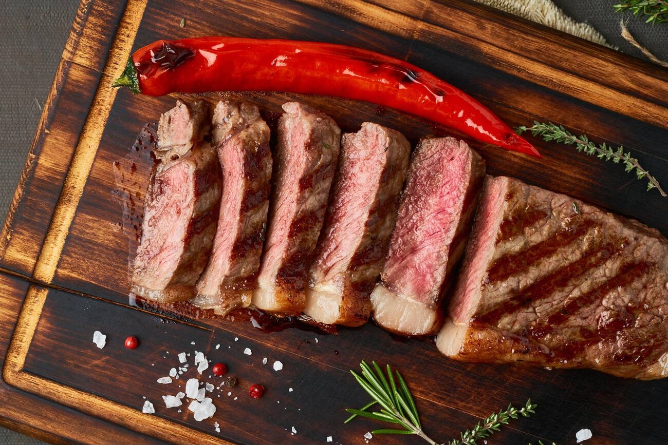 Juicy sliced steak on a wooden cutting board with a red chili pepper and fresh herbs