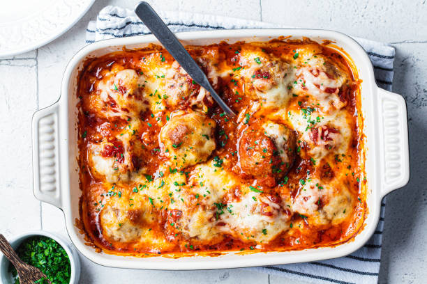 Baked meatballs covered in melted cheese and garnished with parsley in a white dish