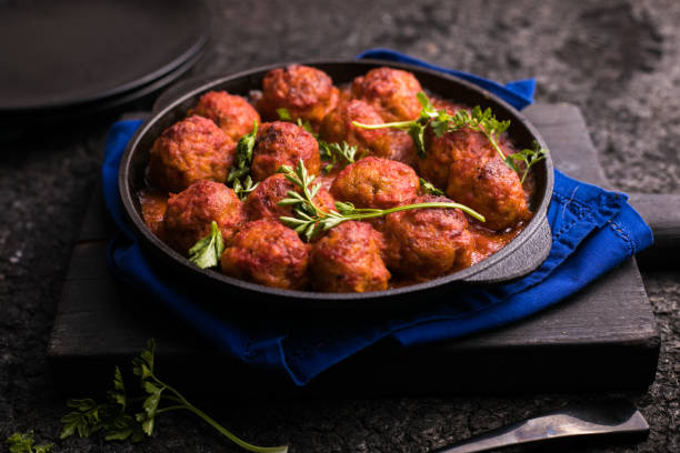 A cast iron skillet filled with meatballs garnished with fresh herbs on a blue napkin.