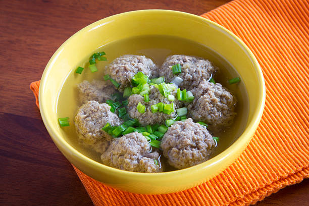 A bowl of meatballs in broth topped with chopped green onions