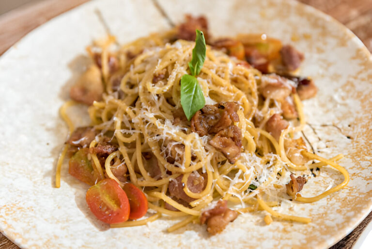 A plate of spaghetti with bacon, cherry tomatoes, and basil garnished with grated cheese.