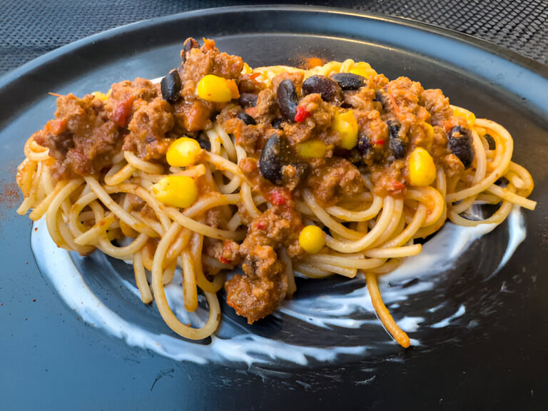 A plate of spaghetti topped with a meat sauce containing ground beef, black beans, and corn.