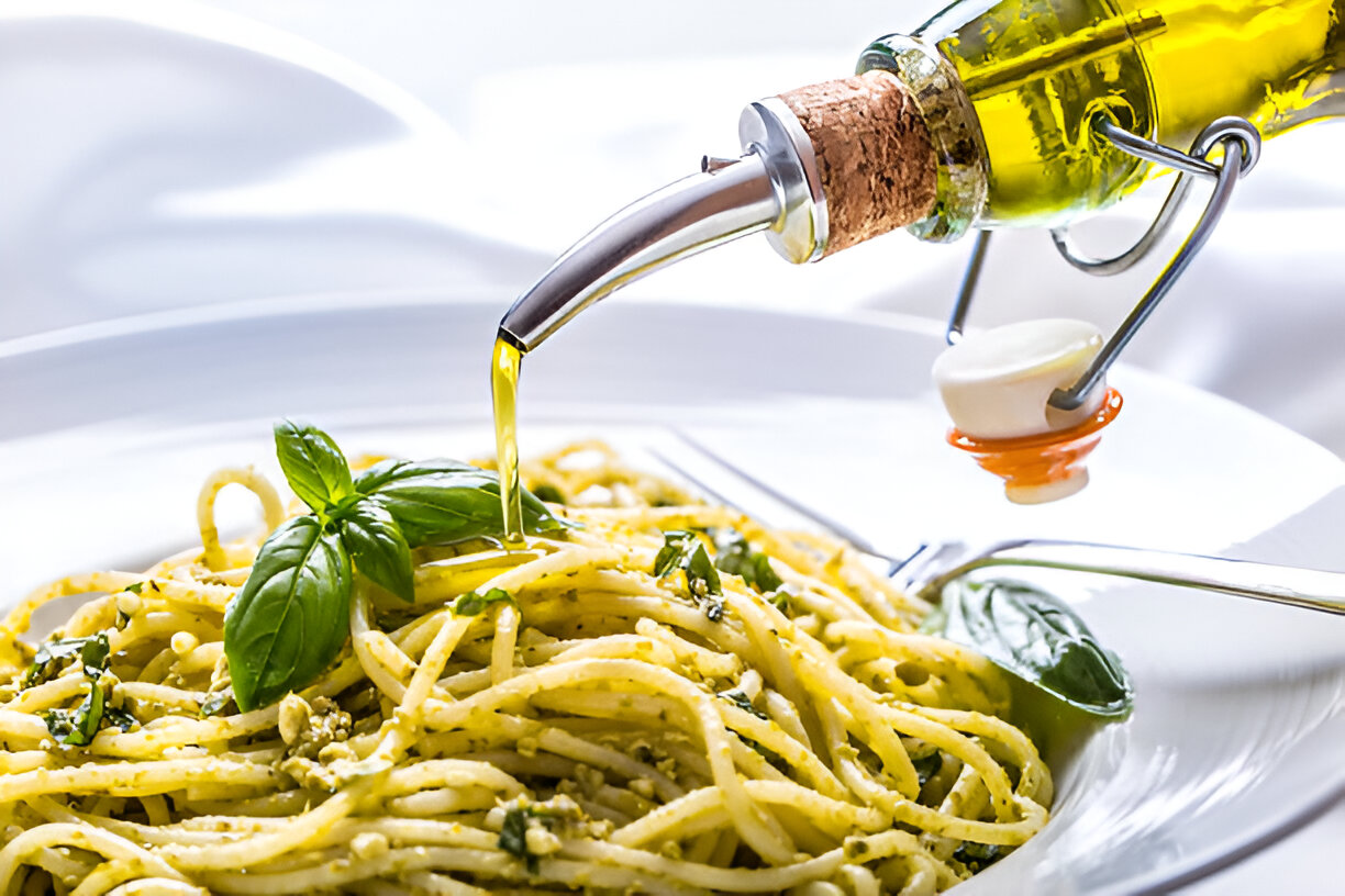 A close-up of a plate of spaghetti topped with basil and drizzled with olive oil from a glass bottle.