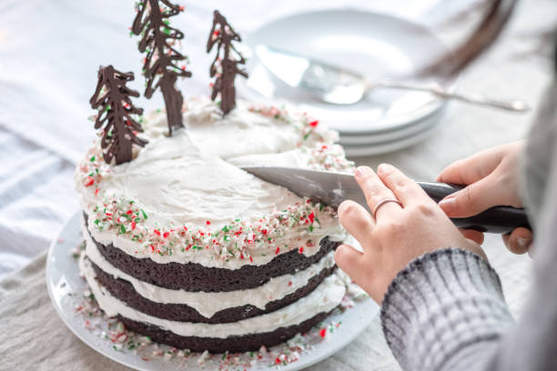 A person cutting a decorated chocolate cake with festive tree decorations on top.