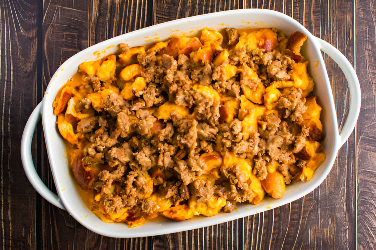 Baked casserole dish filled with cheese, sausage, and biscuit pieces on a wooden table.