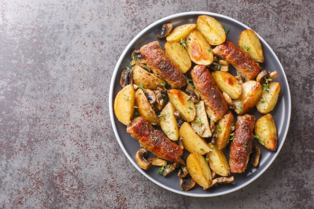 A plate of roasted potatoes, sausages, and mushrooms garnished with herbs.