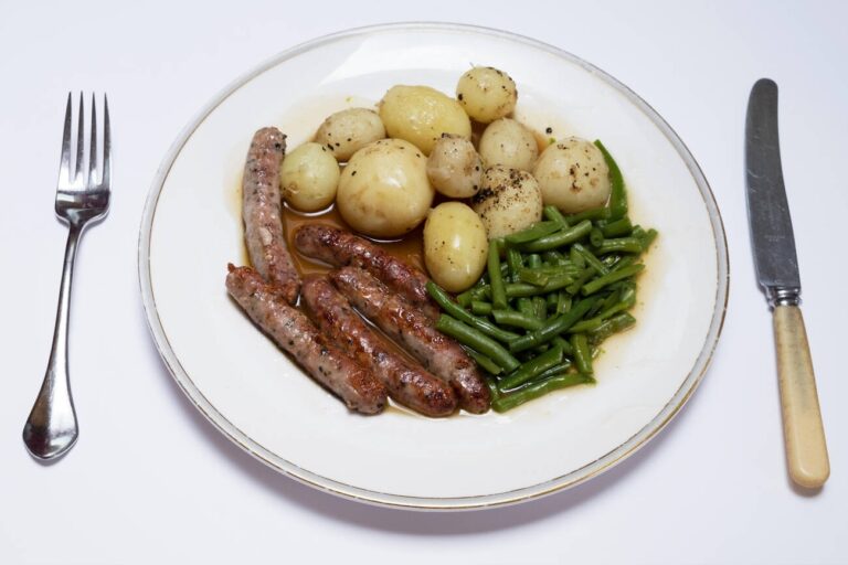 A plate of sausages, boiled potatoes, and green beans served with gravy.