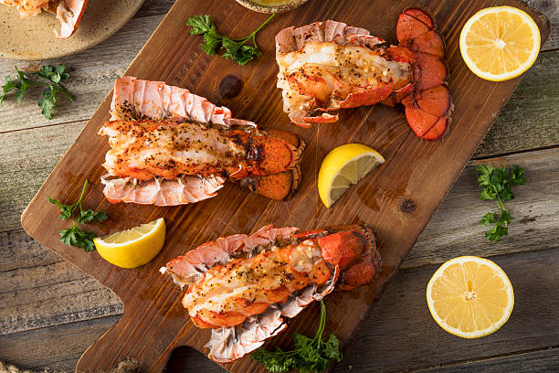 Grilled lobster tails served on a wooden platter with lemon slices and parsley