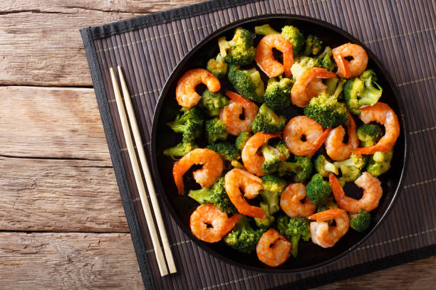 A plate of shrimp and broccoli stir-fry on a wooden table with chopsticks