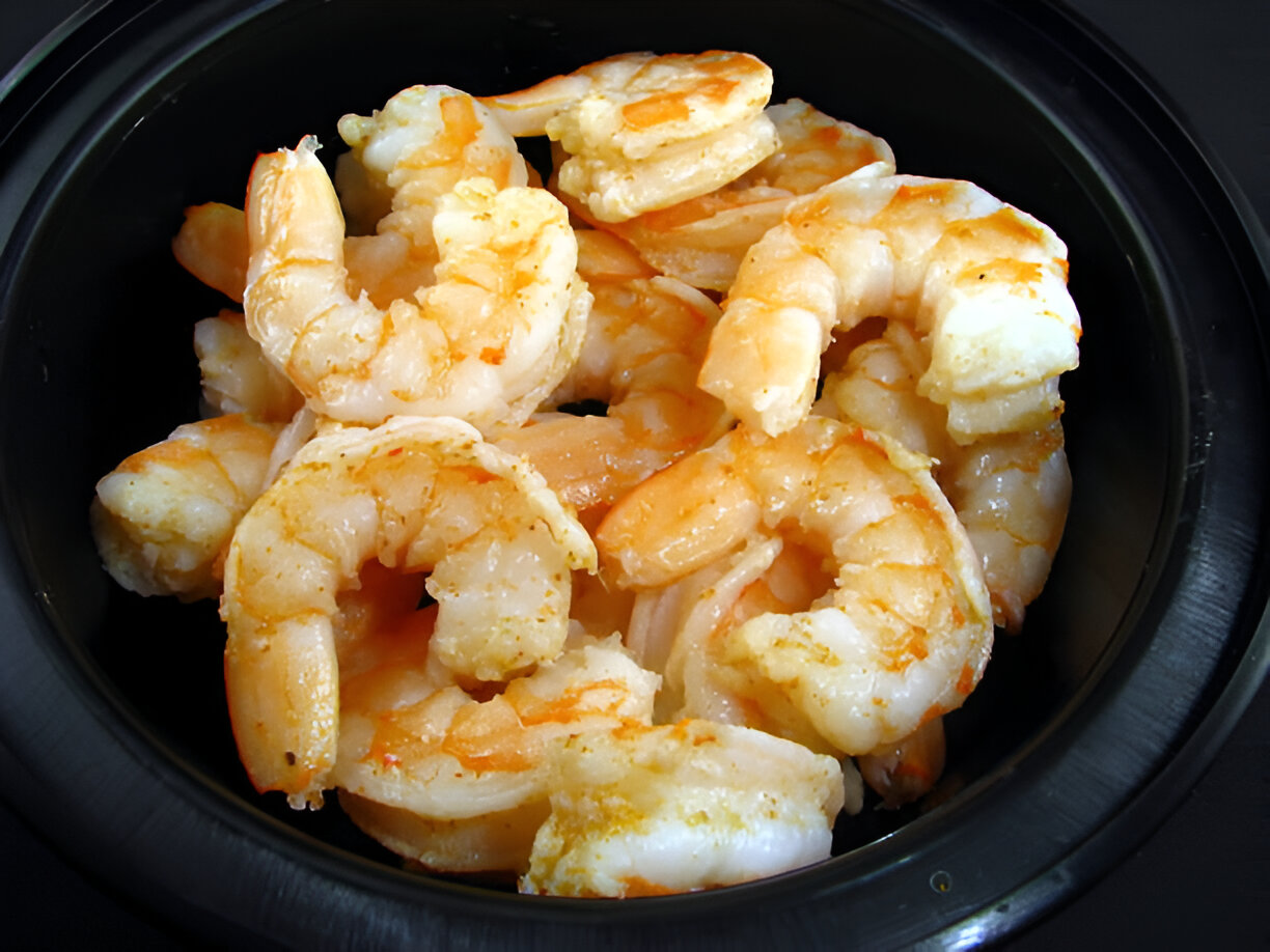 A bowl filled with cooked shrimp in a seasoned orange sauce.