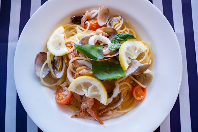 A plate of seafood pasta topped with lemon slices and fresh basil leaves.