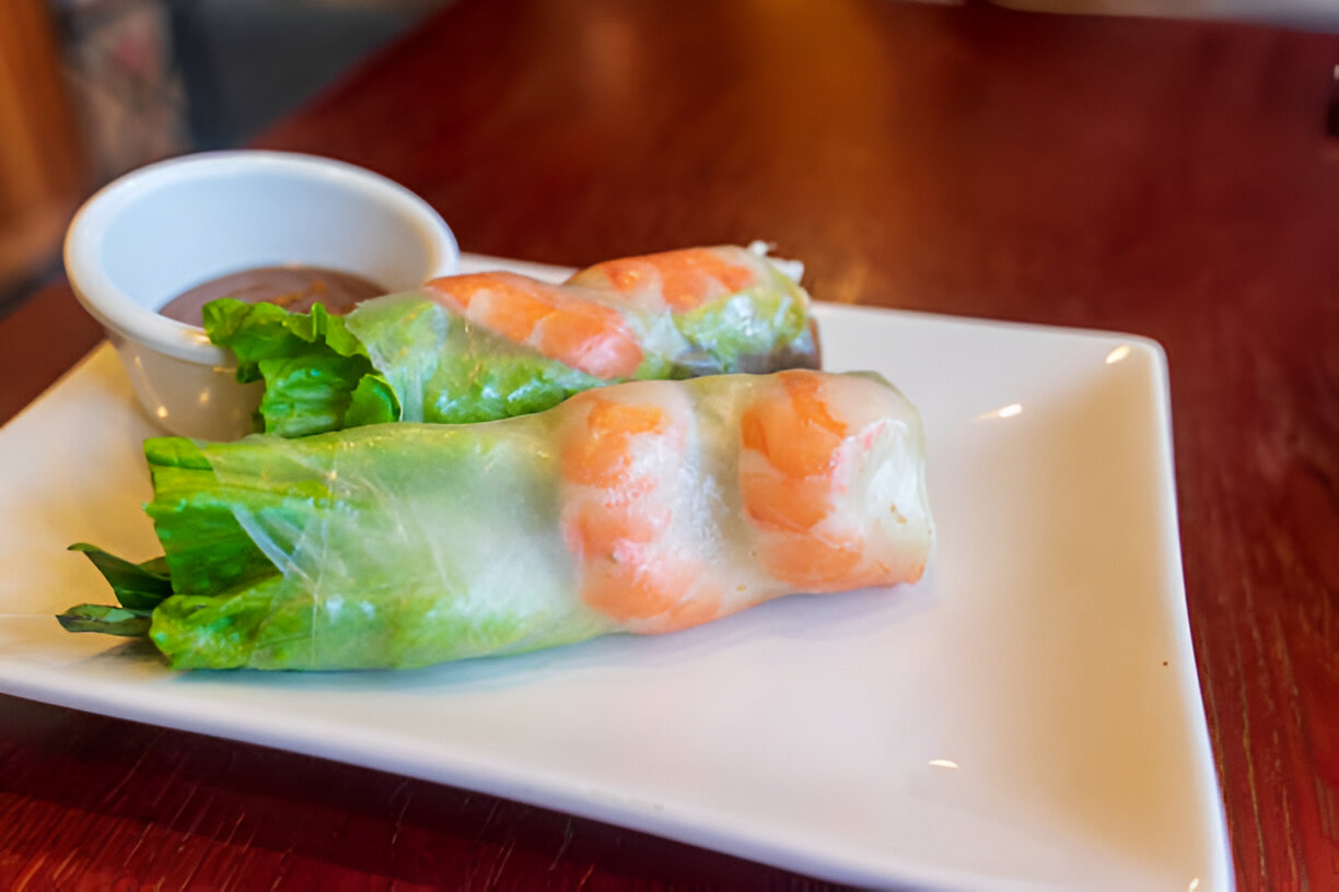 Two fresh spring rolls with shrimp and vegetables, served with a small dish of dipping sauce.