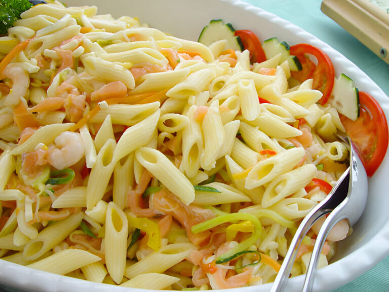 A close-up of a pasta salad with penne pasta, shrimp, and colorful vegetables in a large serving dish.