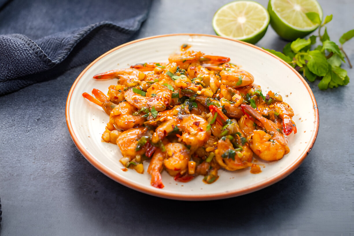 A plate of spicy shrimp garnished with herbs and served with lime wedges.