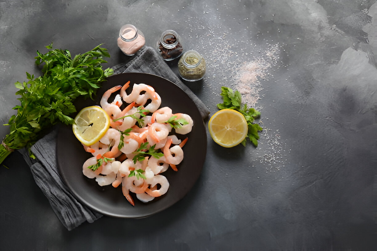Plate of shrimp garnished with fresh parsley and lemon slices on a dark surface.