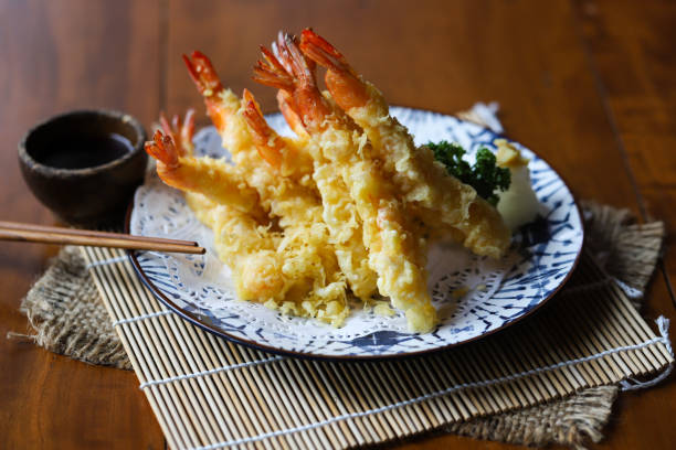 A plate of crispy tempura shrimp served with dipping sauce and garnished with greens.