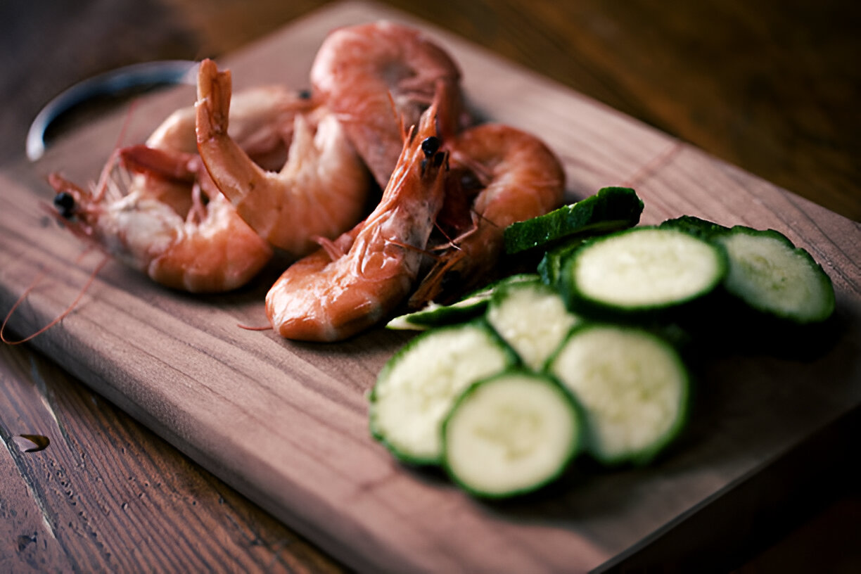 Freshly cooked shrimp and sliced cucumbers on a wooden chopping board