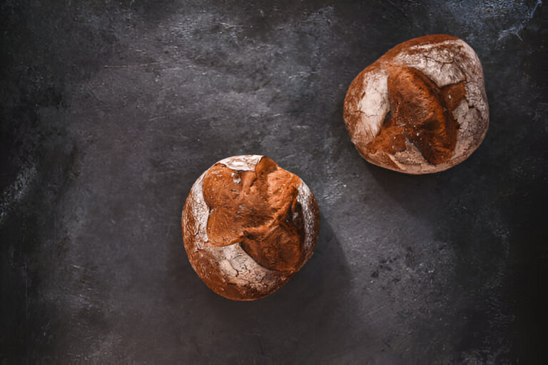 Two rustic bread rolls on a dark surface