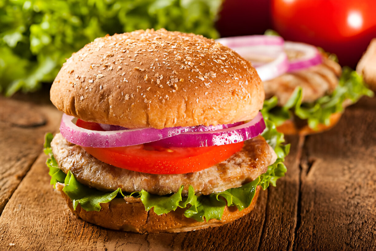 A close-up image of a hamburger with lettuce, tomato, red onion, and a sesame seed bun.