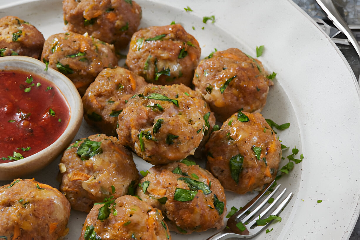 A plate of meatballs garnished with herbs, accompanied by a small bowl of red sauce