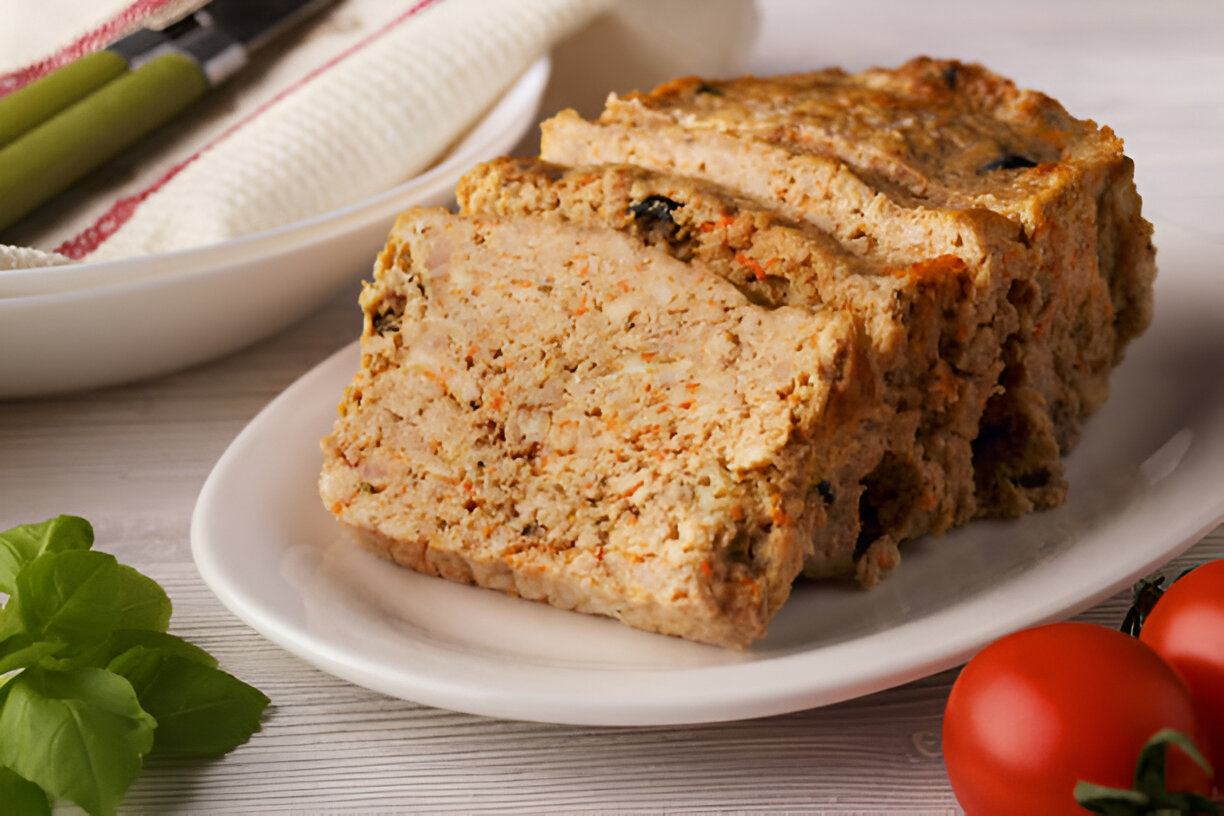 Slices of meatloaf arranged on a white plate with fresh herbs and cherry tomatoes on the side